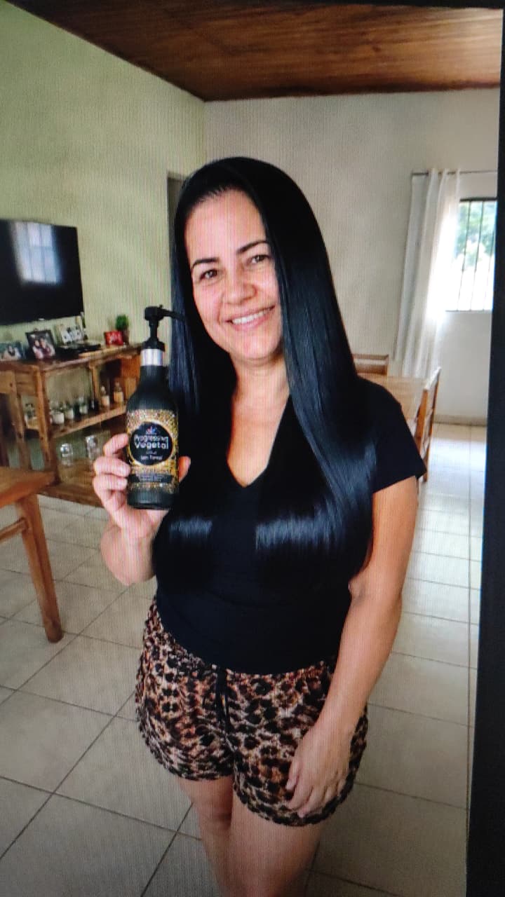 Cliente sorridente segurando o frasco da progressiva com o cabelo liso e brilhante